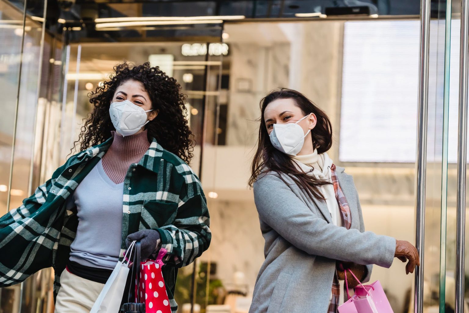 female friends in masks walking out of shopping center