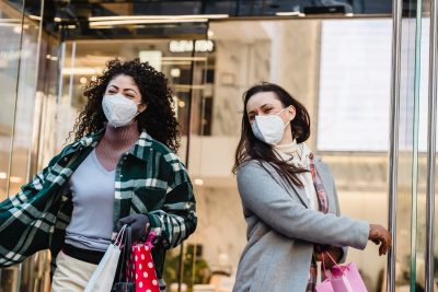 female friends in masks walking out of shopping center